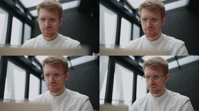 戴着视觉眼镜的时尚男人正在使用笔记本电脑，专注而严肃的脸