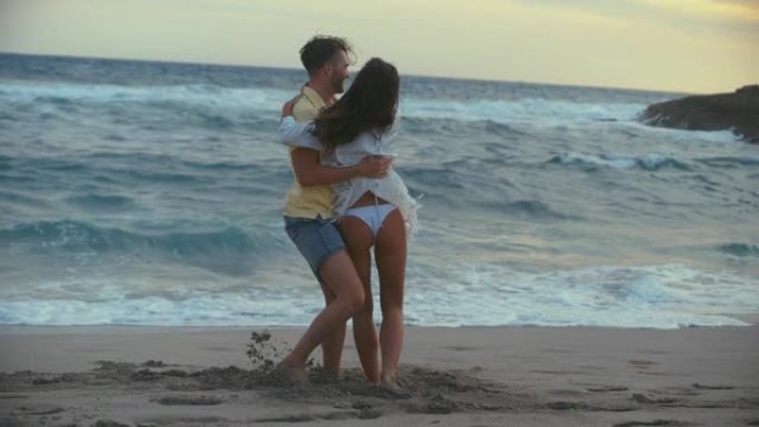 海滩上浪漫的旋转。充满爱心的男朋友在空中举起女友并四处旋转