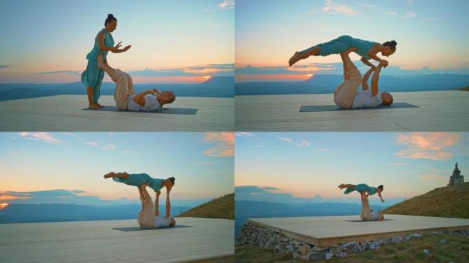 CS男人和女人做瑜伽姿势，男人在日落时用腿在山上抬起女人