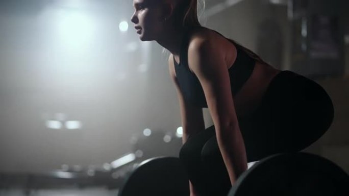 金发碧眼的运动女人在健身房努力工作，举起杠铃，在训练健身馆慢动作
