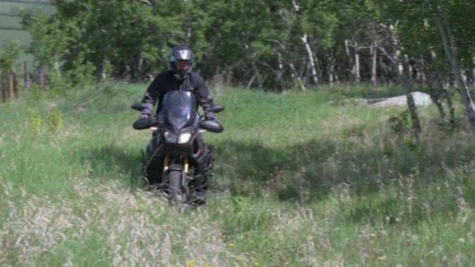 摩托车骑手穿过深草穿过乡村草地