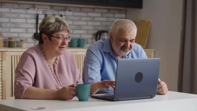 老人和女人正在学习一起使用笔记本电脑，周末坐在家里的厨房里，按下按钮，看着显示屏