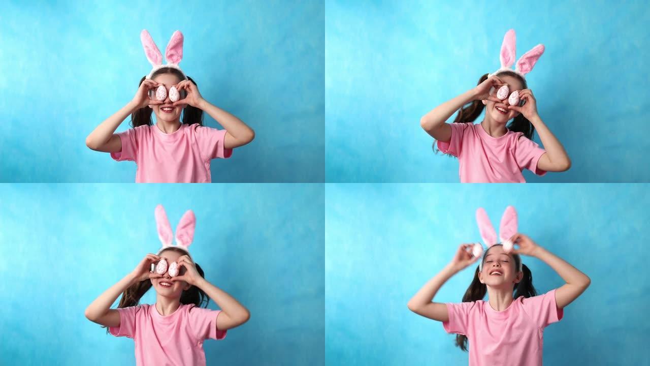 可爱的少女，蓝色背景上有复活节兔子的耳朵，把复活节彩蛋放在她的眼睛附近