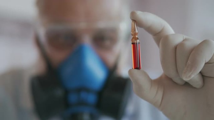 一位科学家戴着蓝色呼吸器和防护眼镜的极端特写镜头，这是一种冠状病毒疫苗的开发者，手持红色安瓿。医生看