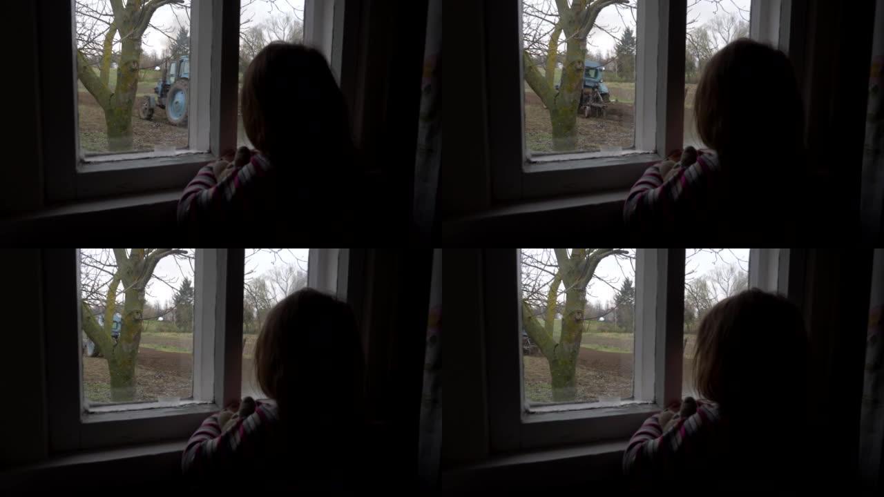 女童透过农村房的窗户看着拖拉机的工作