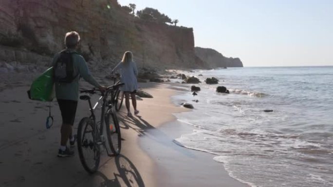 夫妇沿着空旷的海滩推自行车