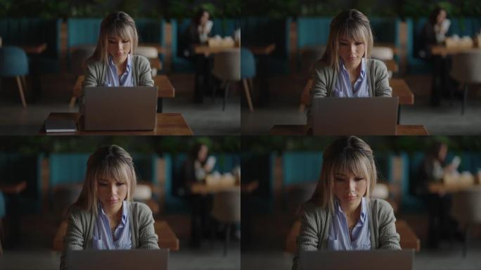 一位亚洲年轻女子坐在咖啡馆里一边工作一边看着笔记本电脑屏幕