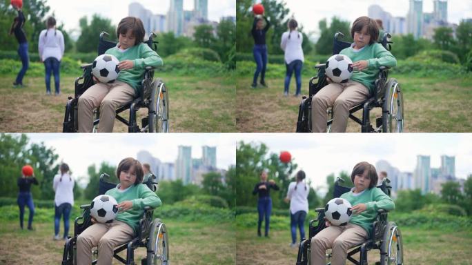 绝望的白人残疾男孩坐在轮椅上，拿着球看着相机，表情悲伤，朋友们在背景慢动作中玩耍。沮丧的孩子在公园摆