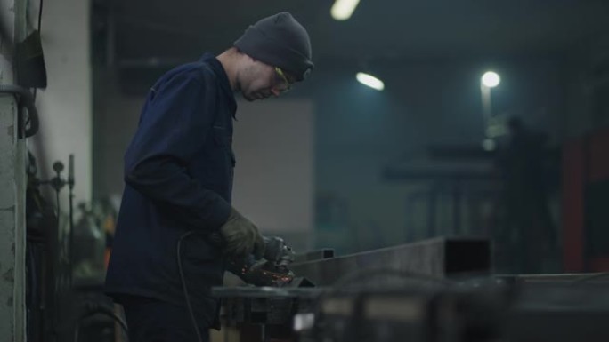 一名工厂工人在慢动作中与金属飞火一起工作。一名戴着防护眼镜的人从事金属研磨抛光和剥离钢金属结构的工作