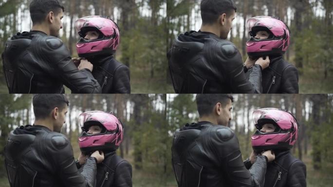 中东男子系好她的粉红色摩托车头盔时，年轻的高加索女友向男友微笑的肖像。爱跨种族快乐的摩托车手夫妇准备