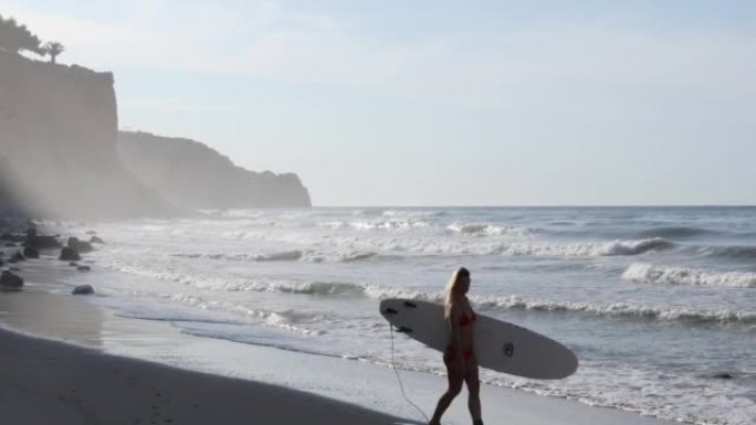 日出时分，年轻女子拿着冲浪板冲浪