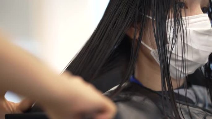 亚洲女人她在美容院穿着保护性弥撒，她卷曲和拉直头发。
