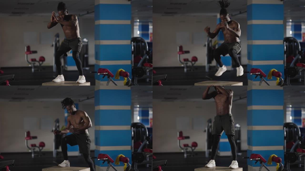 宽投篮强壮的非洲裔美国运动员跳上健身房立方体做深蹲。肌肉持久的英俊健美男子在室内训练的肖像。运动和男