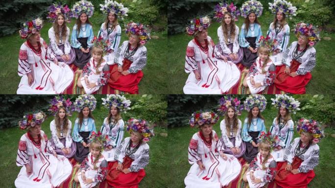 高角度视角漂亮的乌克兰小女孩坐在春夏草地上看着相机，一群穿着民族服装的漂亮年轻女子唱歌。乌克兰的概念