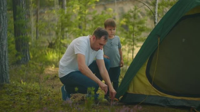 这个男孩帮助他的父亲在森林里搭建和组装帐篷。教孩子，一起在帐篷营地旅行