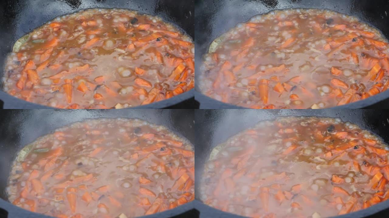 洋葱和胡萝卜在铸铁大锅中油炸。有烟和蒸汽。在户外烹饪。特写。