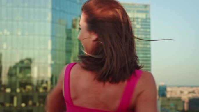 穿着粉色衣服的女人在屋顶上跳舞。大笑和旋转