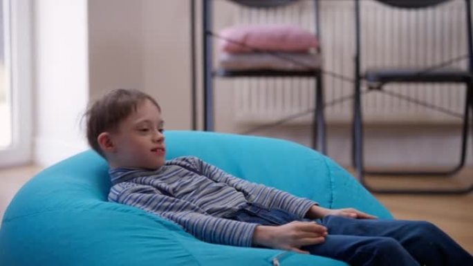 快乐的自闭症男孩躺在家里舒适的包椅上扔泰迪熊。笑高加索孩子的肖像，精神障碍在室内玩得开心。舒适和自闭