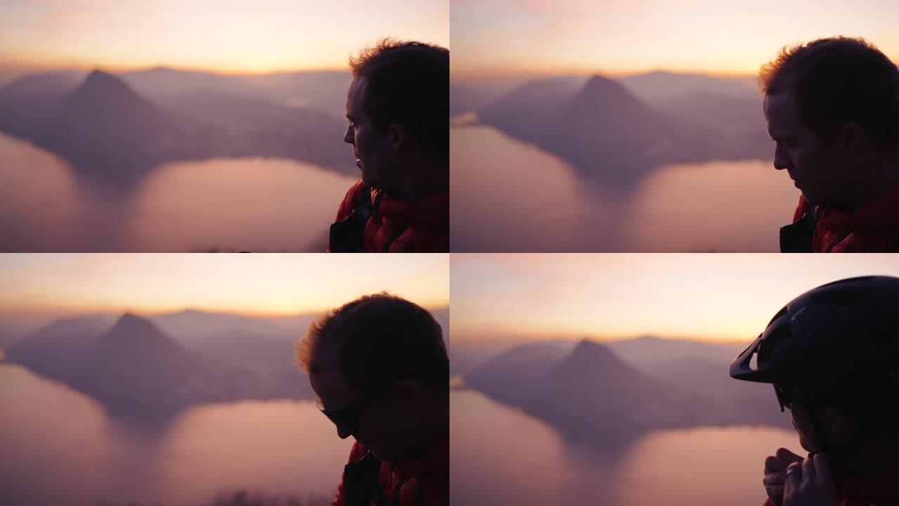 山地车手坐在山顶上，在日落时眺望下方的城市