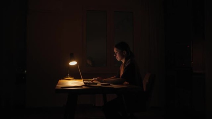 晚上在灯下的女人在黑暗中在家工作。工作截止日期的晚上时间是紧迫的截止日期。