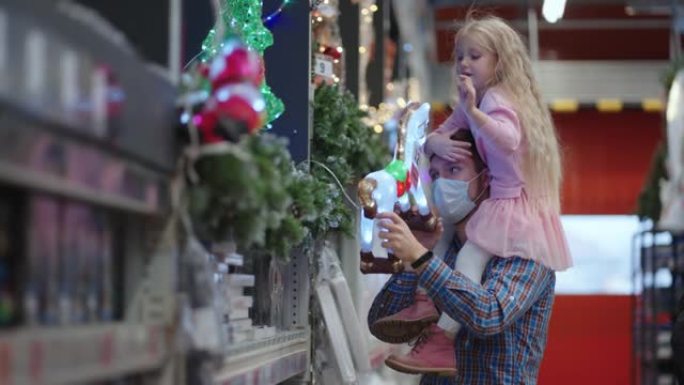 爸爸和女儿在商店里选择带有圣诞树玩具的装饰品和花环。圣诞花环和装饰