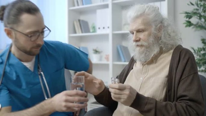 男性照顾者向老年患者提供药丸和一杯水，医疗机构