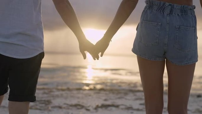 手牵手的夫妇。日落海滩上紫色和橙色天空的深色轮廓。特写