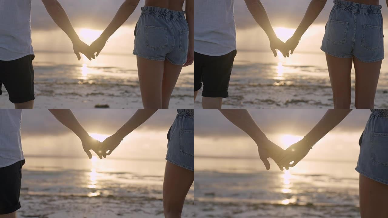手牵手的夫妇。日落海滩上紫色和橙色天空的深色轮廓。特写