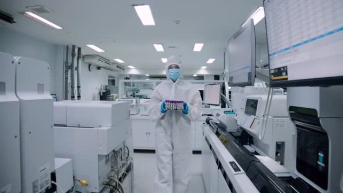 科学家在实验室的无菌室内行走并穿着防护服，手持血液试管。