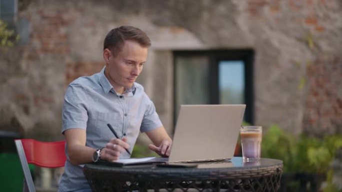 一个坐在街头咖啡馆里的男人在笔记本上远程写笔。在笔记本电脑上工作。一名男子在笔记本电脑上远程工作