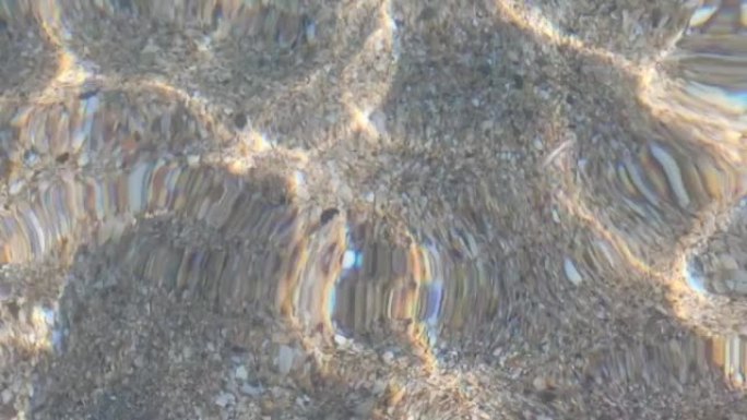 太阳的眩光反映在最纯净的透明海水特写，沙质海底。由于微风，小浪冲入水中