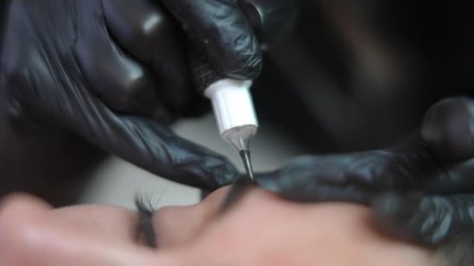 纹身大师的特写手使用微刀片笔在年轻白人女性的眉毛皮肤中注入墨水。在美容院做永久化妆的客户的微刀片纹身