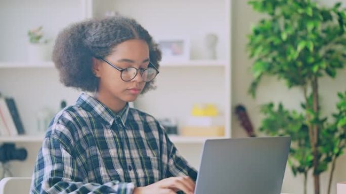 聪明的黑人少女在眼镜上打开笔记本电脑，为学校做作业