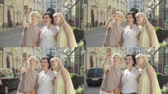 三名快乐的成年女性在外国城市街道上自拍的中景。积极的高加索游客喜欢出国旅行的肖像。开朗的金发和黑发朋