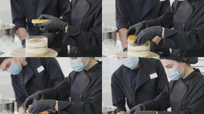 相机从女性的双手向上移动，将烘烤的圆形面团放在蛋饼上，到糖果人和受训者戴着Covid口罩的集中脸。厨