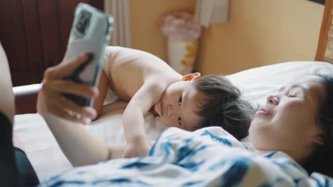 亚洲母亲在家中与婴儿在智能手机上自拍