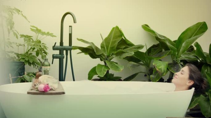 年轻女子在浴室内郁郁葱葱的绿色花园里泡泡浴