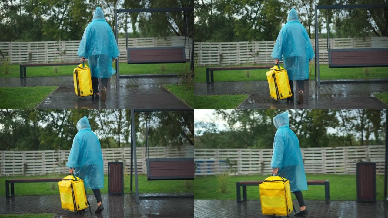 在城市公园转弯时，穿着雨衣的宽镜头快递员带着黄色背包行走。现场摄像机跟随年轻的白人男子在雨天在户外运
