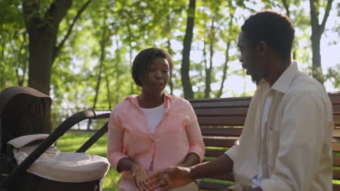 年轻的黑人父母在谈论育儿职责，坐在公园的长凳上