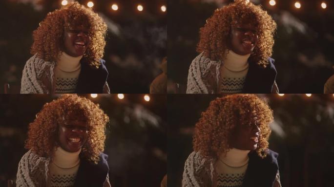 快乐的非洲裔美国妇女的肖像在篝火旁，笑着保持烤棉花糖