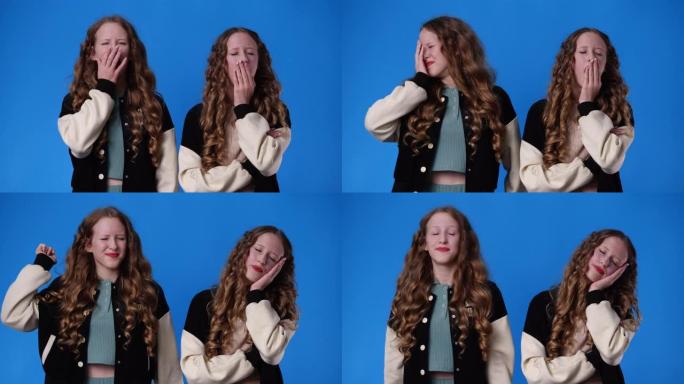 双胞胎女孩在蓝色背景上打哈欠的4k慢动作视频。