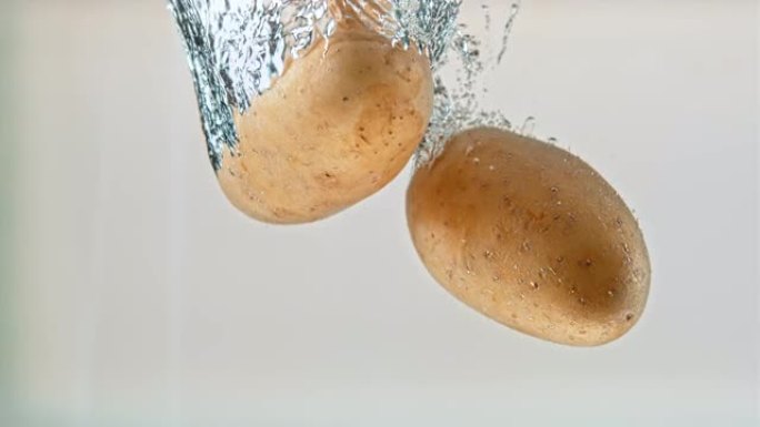 SLO MO LD整个土豆在白色背景下落入水中