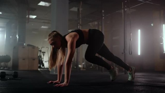 一名女子在健身后的黑暗健身房里做伸展运动，健身女子在黑暗的健身房里锻炼核心肌肉