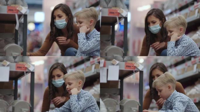 在大流行购物，戴着口罩的女人和儿子在儿童商店选择玩具，年轻的母亲在超市购买商品，预防病毒性疾病