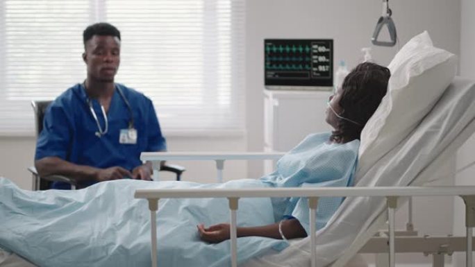 一名男医生正在医院病房里与躺在病床上的病人交谈。连接到氧气和面罩。