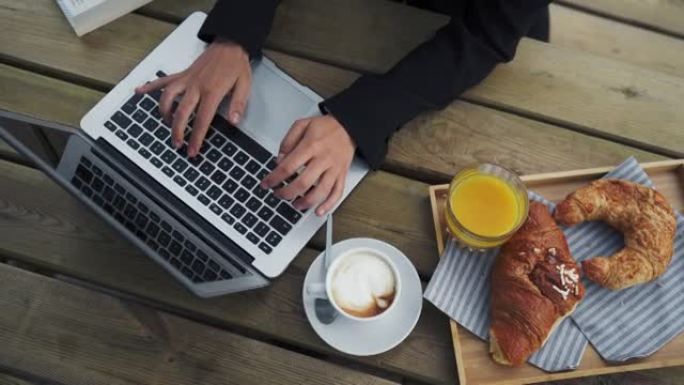 在笔记本电脑上工作的女商人的自上而下的照片，周围有自助早餐和咖啡