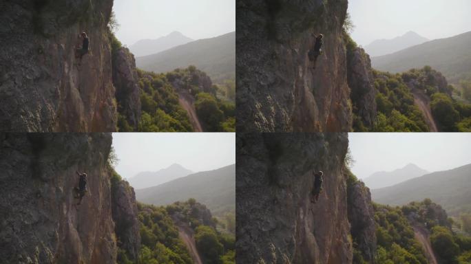 空中无人机拍摄了一名男子在日落时攀爬在红色岩壁上的岩石