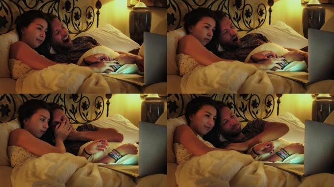 年轻夫妇在床上看电影。使用笔记本电脑和打哈欠
