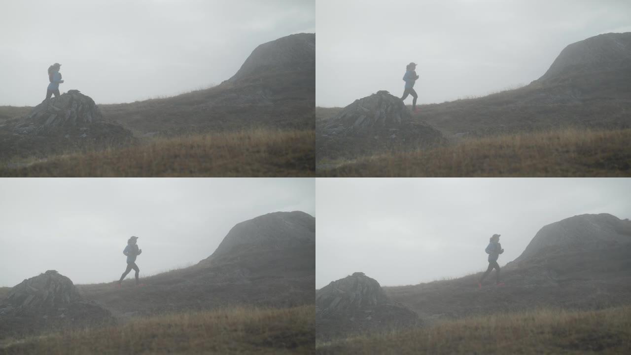 女越野跑运动员在草地上的雾气中奔跑，后面是白雪皑皑的山峰