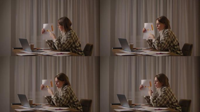 远程工作一个戴着眼镜的年轻女子坐在家里的厨房里进行在线报告时，用笔记本电脑的相机显示了一张图表。视频
